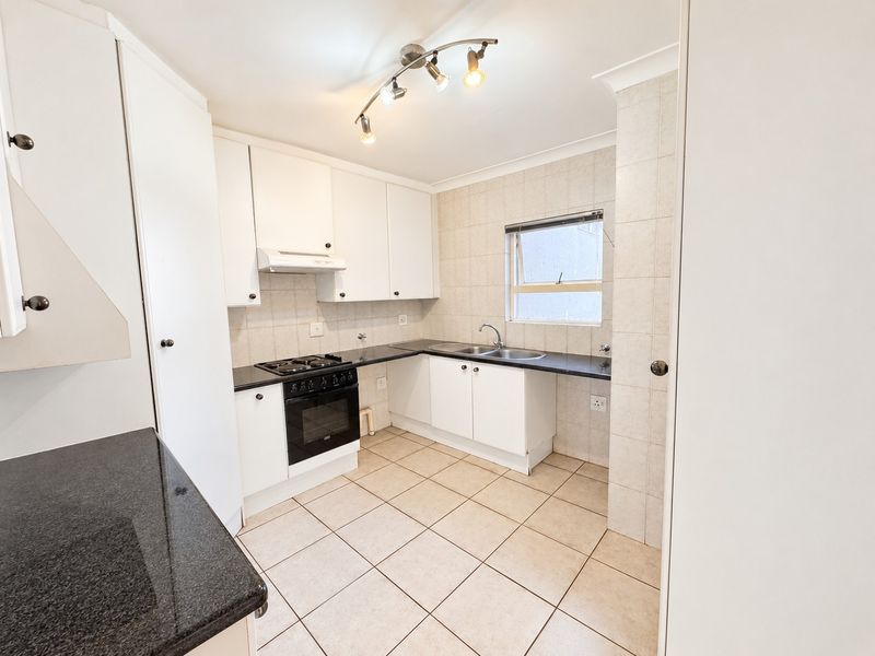 A clean, functional kitchen featuring white cabinetry, dark granite countertops, tiled flooring, and built-in cooking appliances.