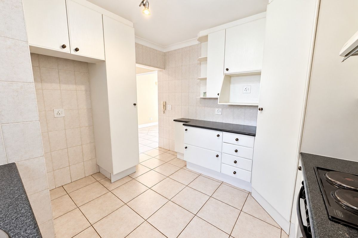 A clean, functional kitchen featuring white built-in cabinetry, dark laminate countertops, tiled backsplash, and ceramic floor tiles.