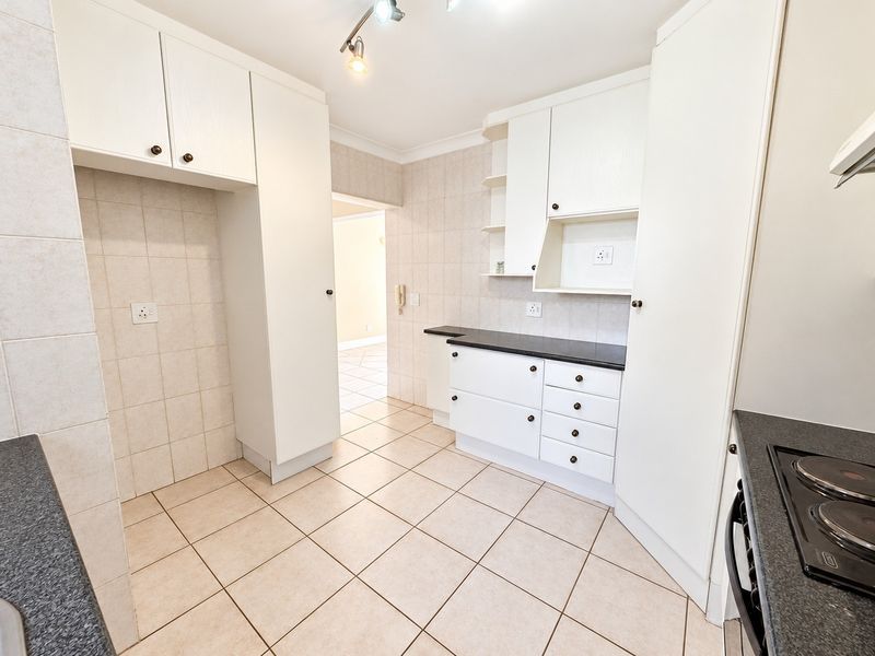 A clean, functional kitchen featuring white built-in cabinetry, dark laminate countertops, tiled backsplash, and ceramic floor tiles.