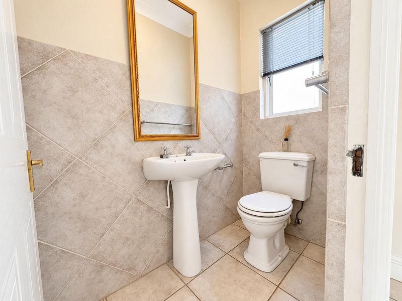 A clean, functional bathroom featuring a pedestal basin, toilet, and neutral tiled finishes throughout.