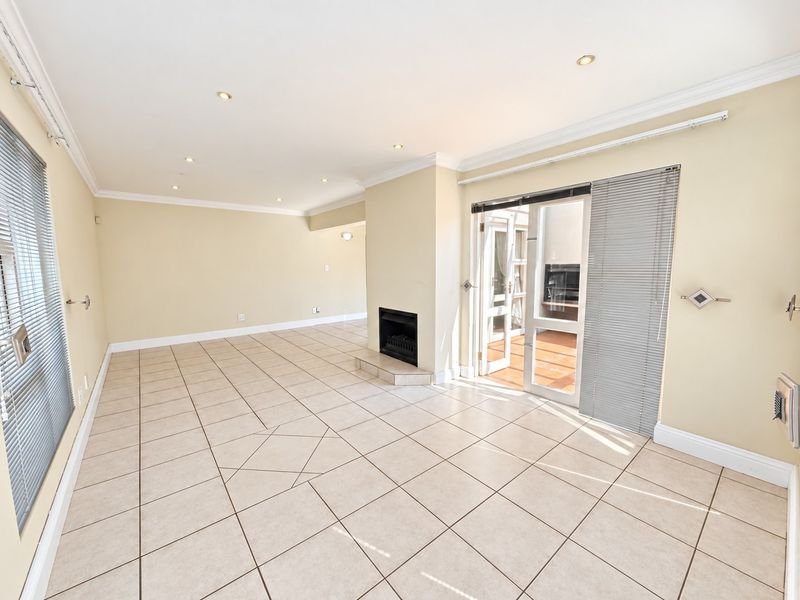 Spacious, light-filled living room featuring neutral tiled flooring, a built-in fireplace, and direct access to an outdoor patio through glass french doors.