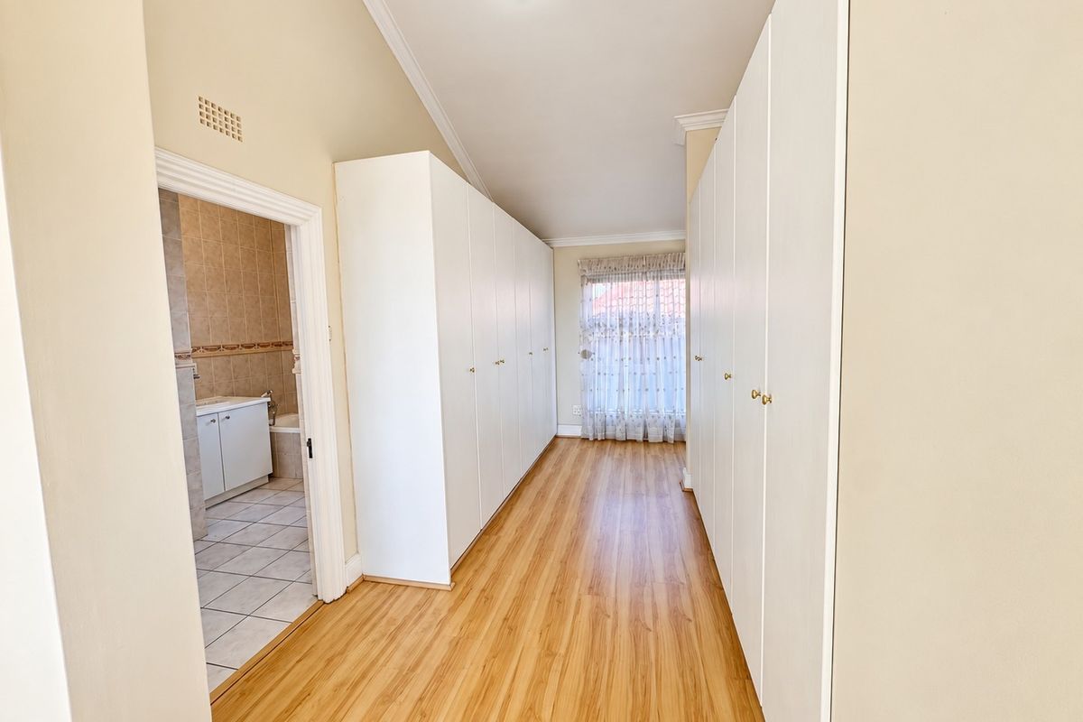 Spacious bedroom featuring extensive built-in cupboard storage, light laminate flooring, and direct access to an en-suite bathroom.