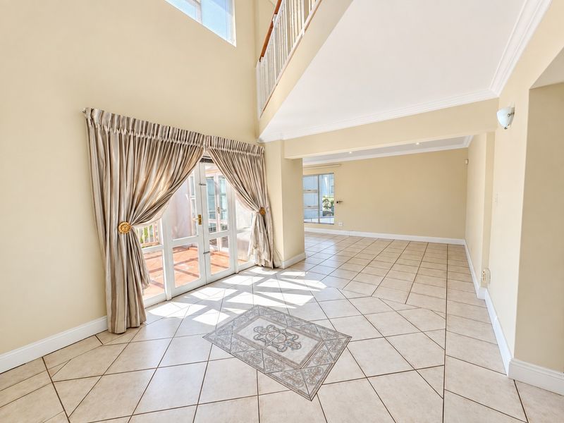 Spacious, light-filled living area featuring double-volume ceilings, tiled flooring with decorative inlay, and direct access to an outdoor patio through French doors.
