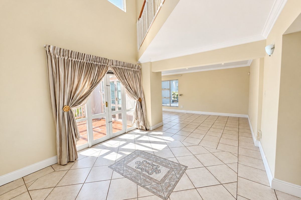 Spacious, light-filled living area featuring double-volume ceilings, tiled flooring with decorative inlay, and direct access to an outdoor patio through French doors.