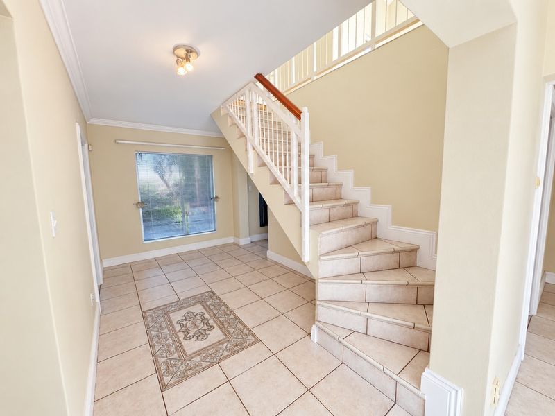 Spacious entrance hall featuring a tiled staircase with a wooden handrail, ceramic flooring with a decorative inlay, and natural light from a large window.