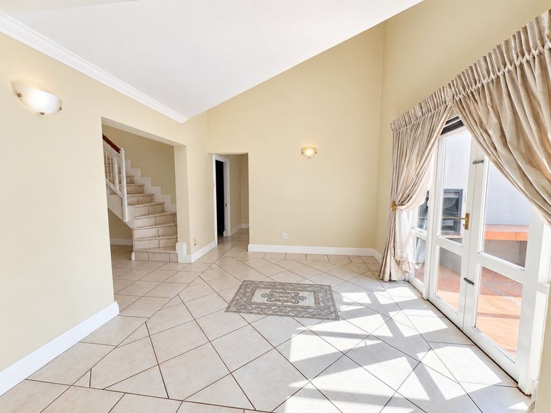 Spacious living area featuring vaulted ceilings, tiled flooring, and direct access to an outdoor patio through glass french doors.