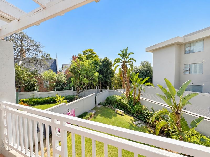 A view from a balcony overlooking a private garden area with established landscaping, boundary walls, and electric fencing.