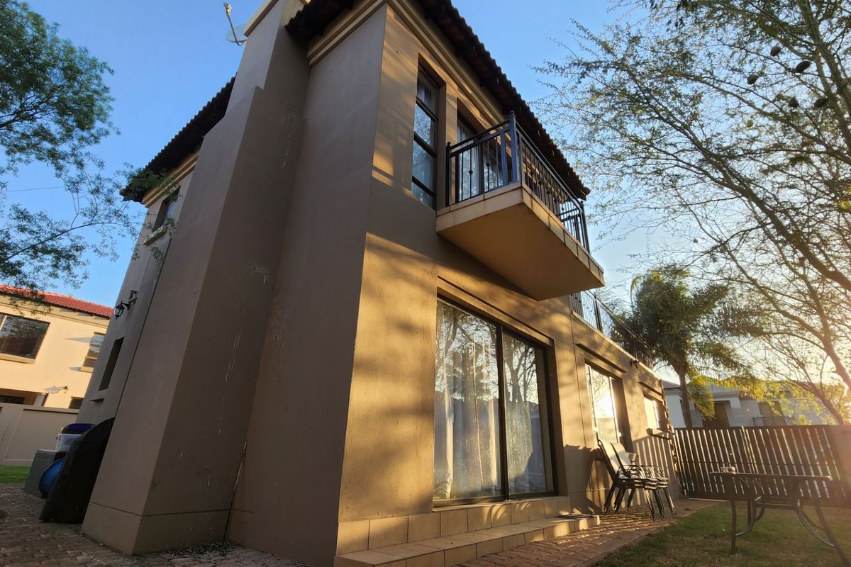 Rear elevation of a multi-story house featuring a private balcony with wrought iron railing and ground-level sliding glass doors opening onto a patio.