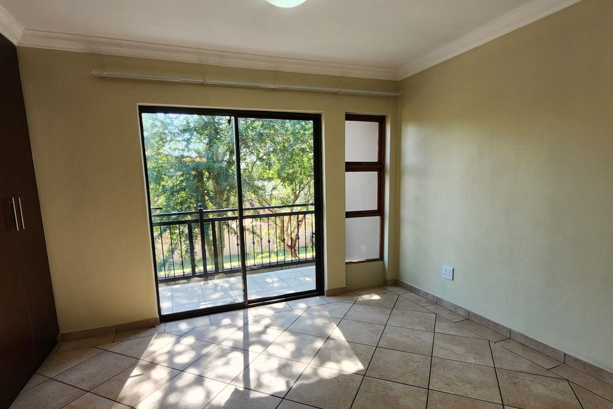 A bright, empty bedroom featuring tiled flooring, built-in cupboards, and a sliding glass door that opens onto a private balcony.