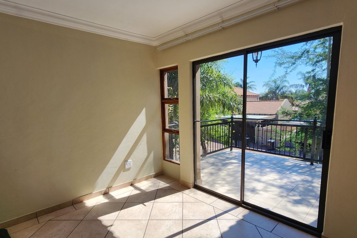 An empty living area featuring tiled floors, cove cornicing, and a large sliding glass door providing direct access to a private balcony.