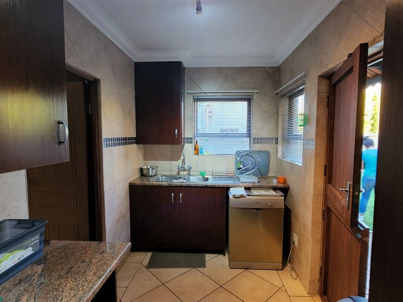 A functional scullery featuring dark wood cabinetry, granite countertops, a stainless steel sink, and tiled finishes with direct access to the exterior.