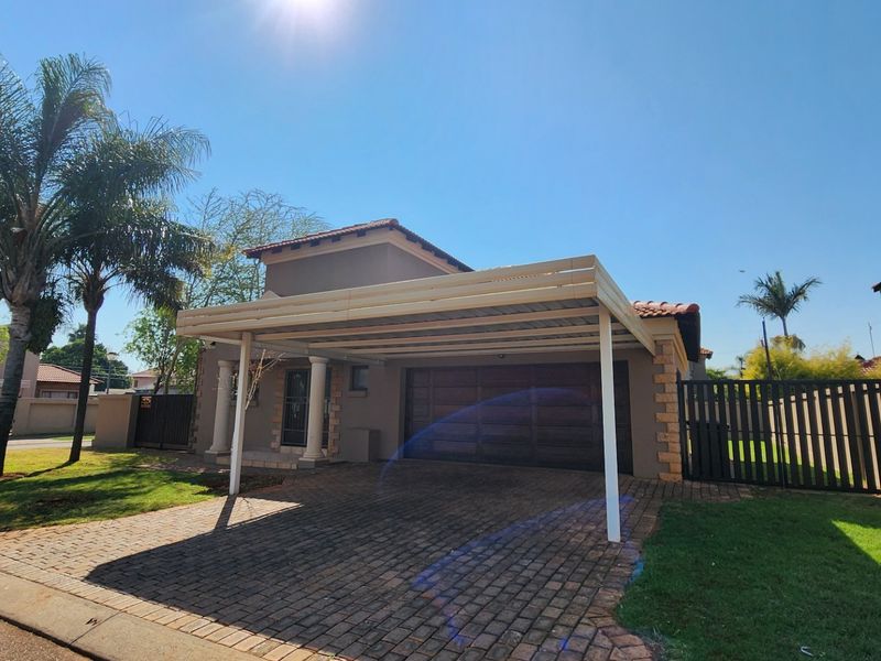 Front exterior view of the property featuring a paved driveway, a covered carport, and a secure garage entrance with boundary walling.