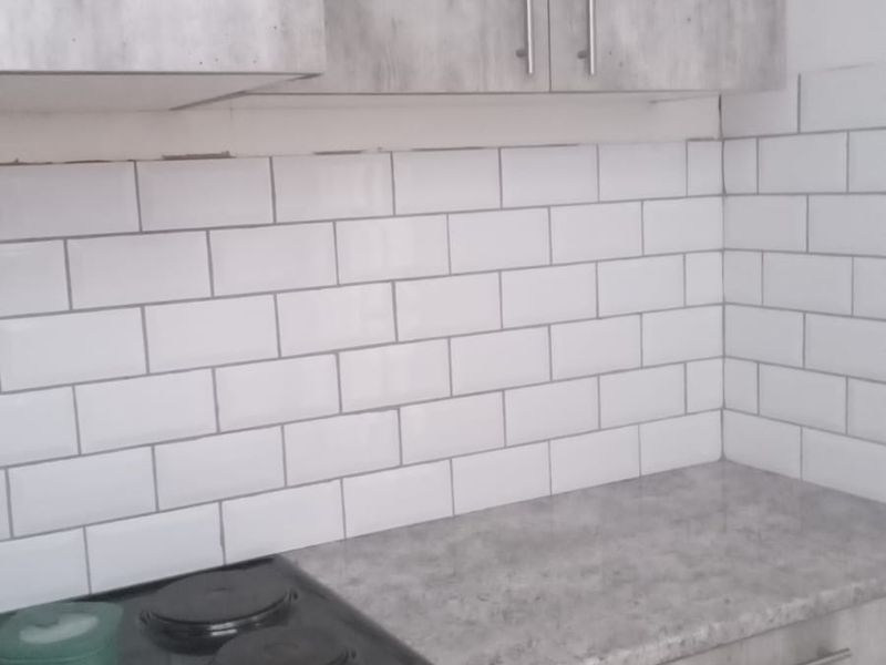 A compact kitchen featuring grey textured cabinetry, a white subway tile backsplash, and a built-in electric oven and hob.