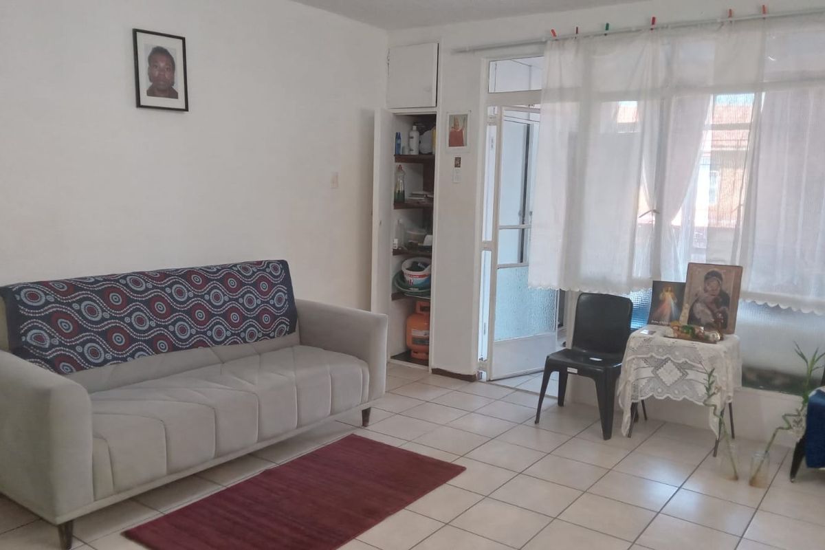 A living room featuring tiled flooring, a built-in storage cupboard, and access to an adjacent outdoor area through a glass panel door.