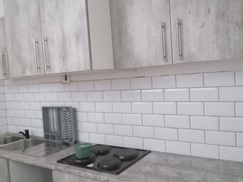 A functional kitchen featuring grey wood-look cabinetry, a white subway tile backsplash, a laminate countertop, and a built-in electric hob.