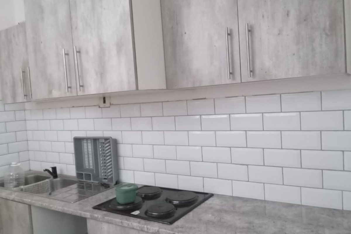 A functional kitchen featuring grey wood-look cabinetry, a white subway tile backsplash, a laminate countertop, and a built-in electric hob.