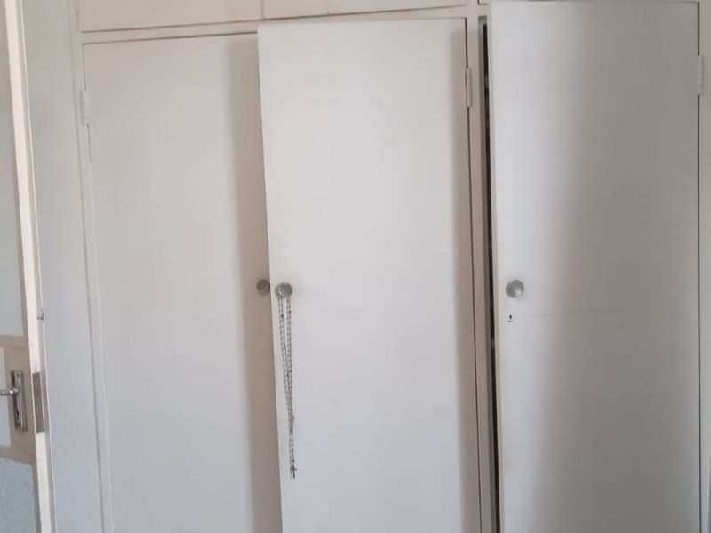 A bedroom featuring white built-in cupboards with overhead storage and tiled flooring throughout.