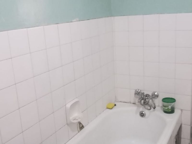 A functional bathroom featuring a standard bathtub with wall-mounted fixtures and partial wall tiling, requiring cosmetic updates to improve its overall condition.