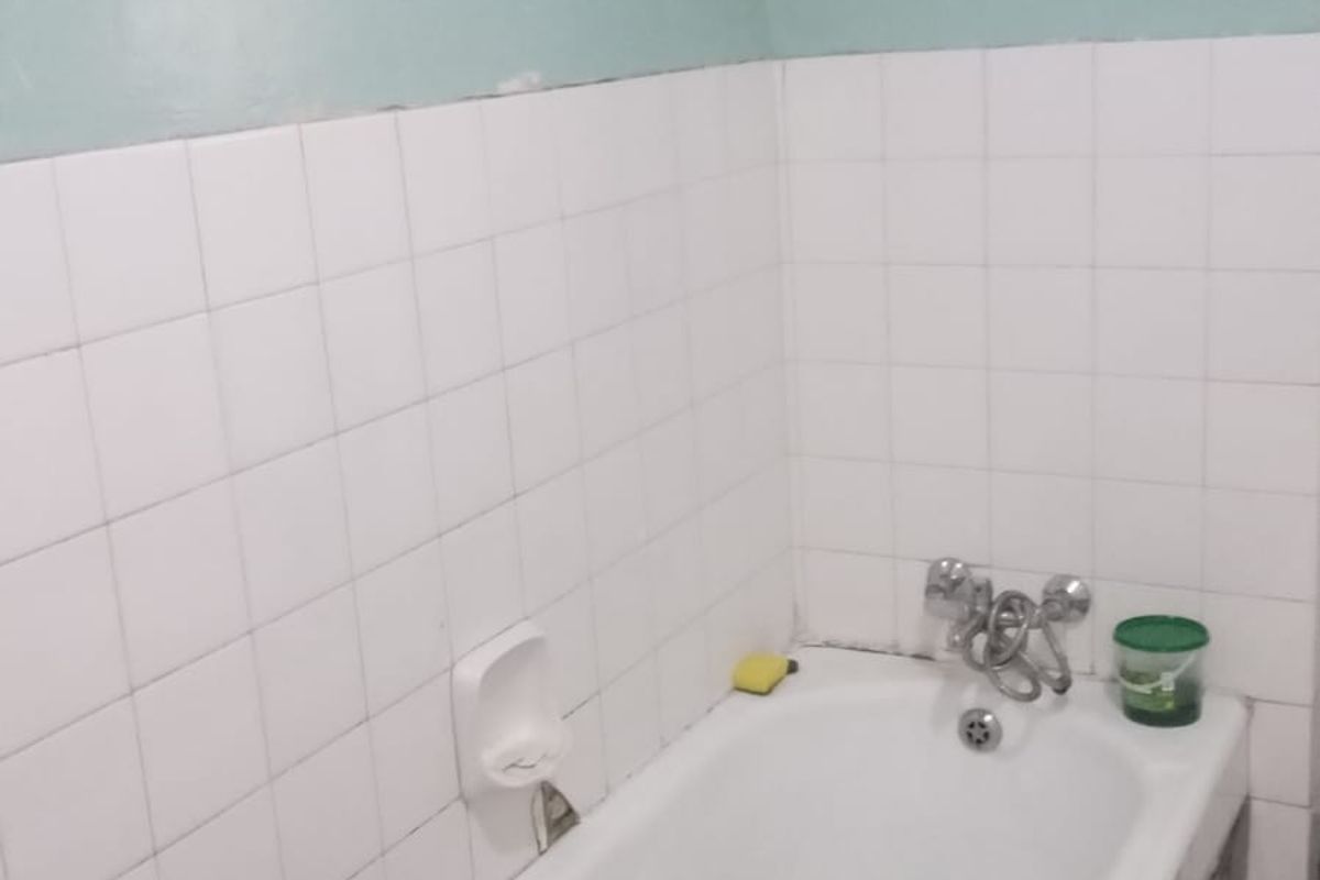 A functional bathroom featuring a standard bathtub with wall-mounted fixtures and partial wall tiling, requiring cosmetic updates to improve its overall condition.
