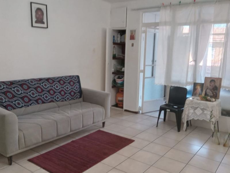 A living room area featuring tiled flooring, a built-in storage cupboard, and access to an adjacent space through a glass panel door.