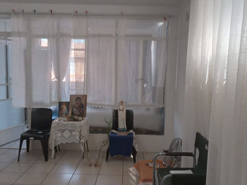 A living area featuring tiled flooring and a large window assembly, providing natural light and access to an adjacent space.