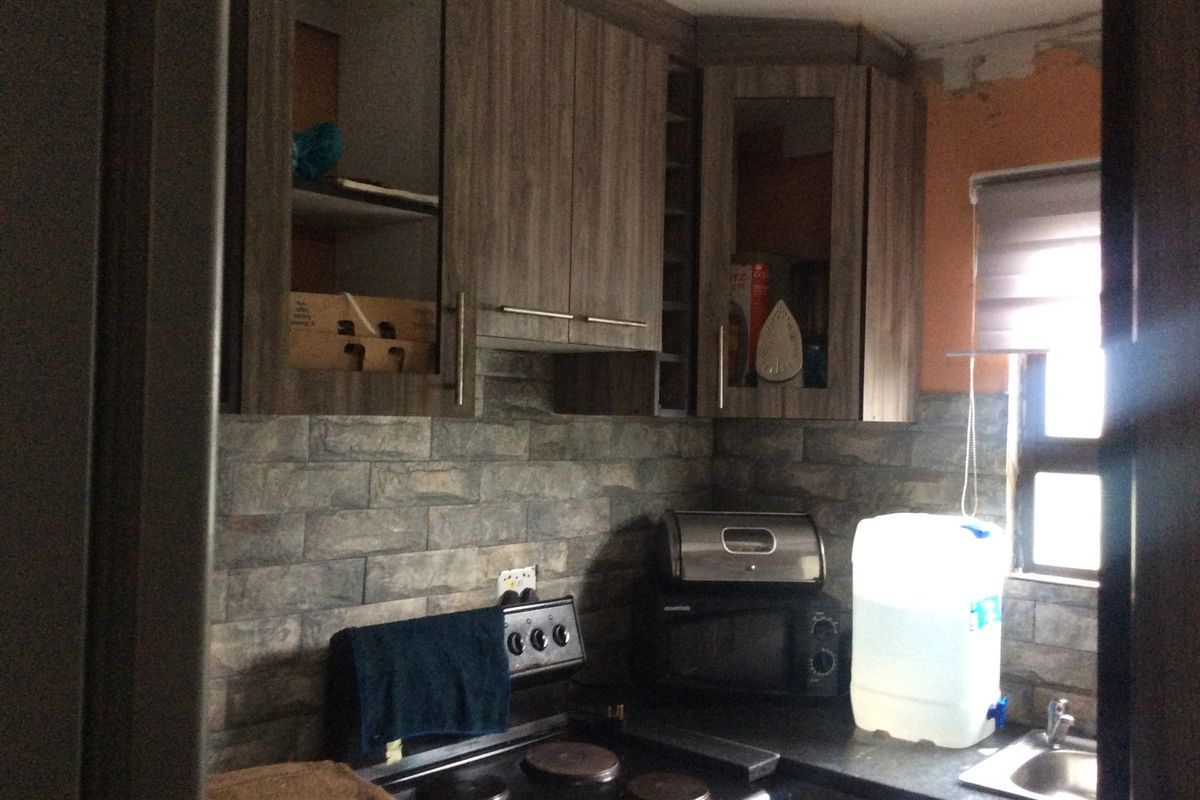 Compact kitchen featuring wood-look cabinetry, stone-style wall cladding, and an electric stove, requiring minor finishing work to the upper wall area.