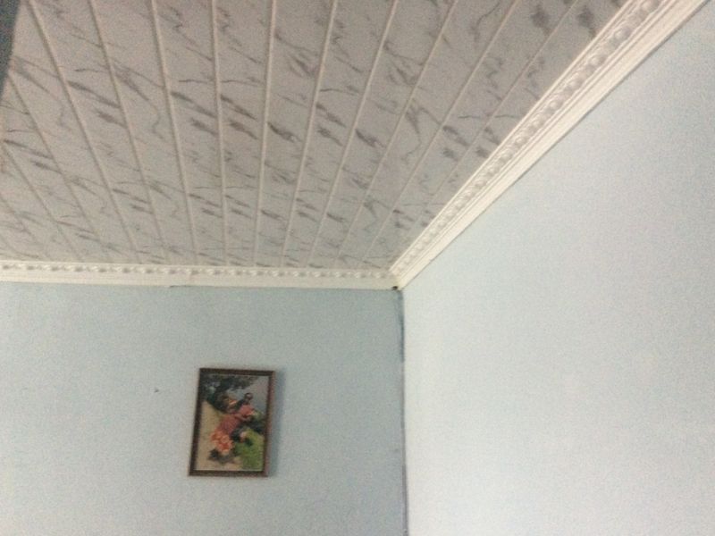 A corner view of a room featuring patterned ceiling panels and decorative molding, showing a visible crack along the wall corner.