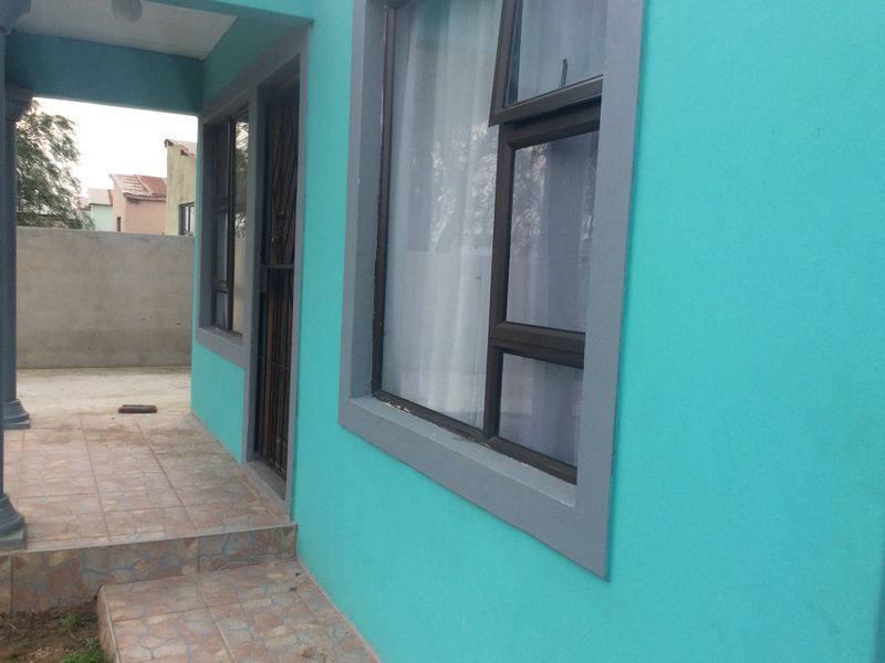 A side view of the house exterior featuring a tiled patio area, aluminium window frames, and a security gate entrance.