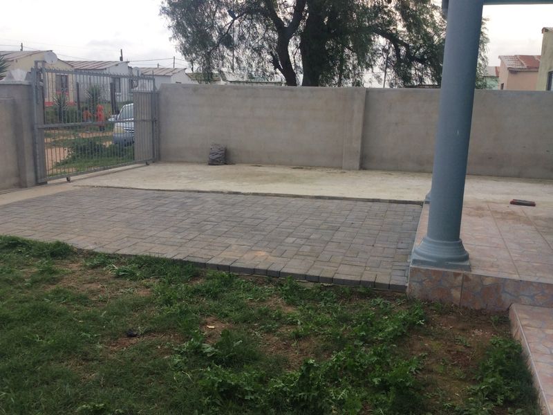 Front exterior area featuring a paved driveway, boundary wall with metal gate, and a tiled porch with a structural column.