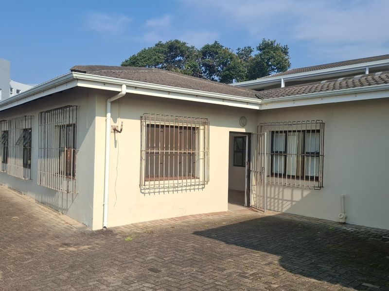 Rear exterior view of the townhouse featuring a paved courtyard area, tiled roof, and security bars on the windows.