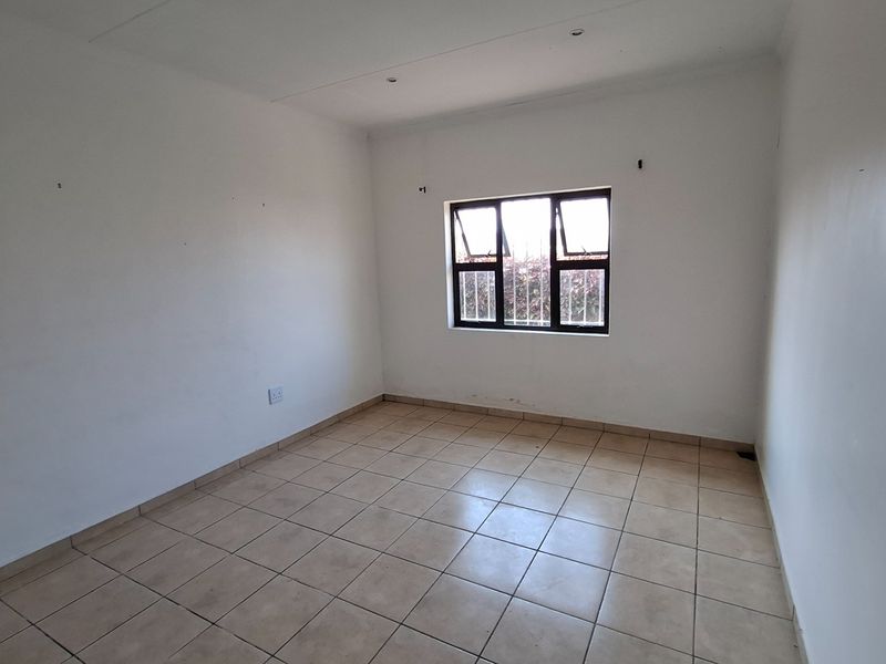 A vacant bedroom featuring neutral tiled flooring, white walls, and a window fitted with security bars.