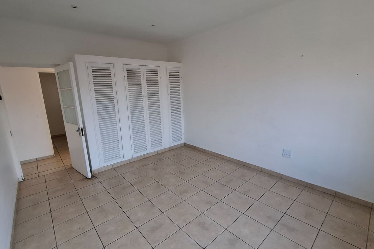 An empty bedroom featuring tiled flooring, built-in louvered cupboards, and recessed ceiling lighting, offering a blank canvas for personalization.