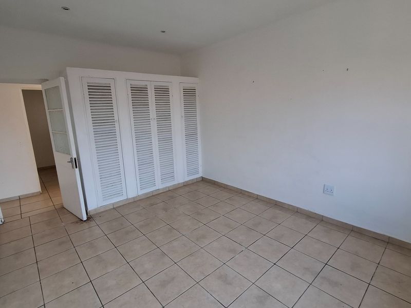An empty bedroom featuring tiled flooring, built-in louvered cupboards, and recessed ceiling lighting, offering a blank canvas for personalization.