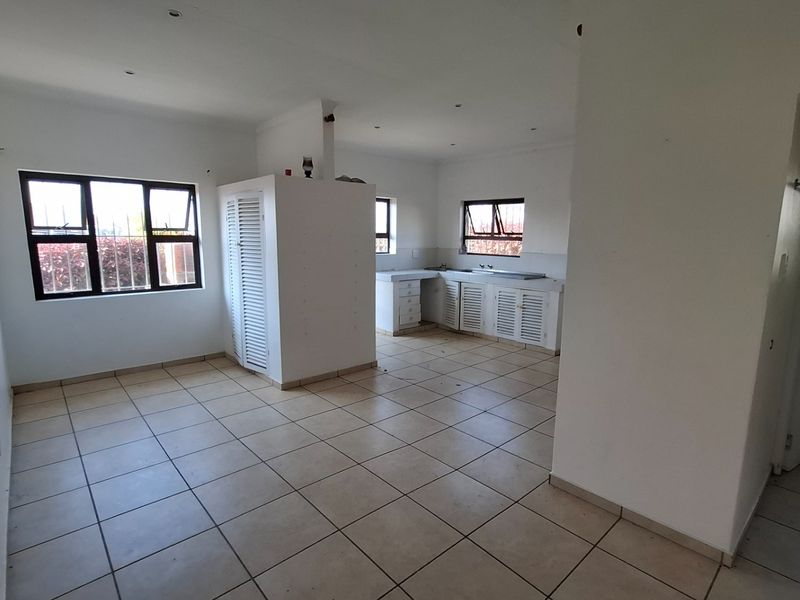 An open-plan living and kitchen area featuring tiled flooring, built-in cabinetry, and security bars on the windows. The space is vacant and ready for renovation.