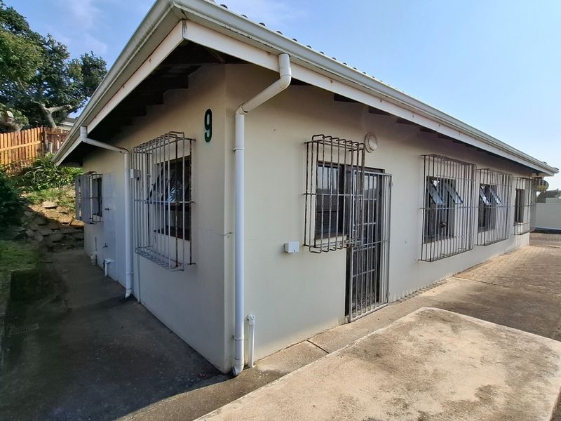 Rear exterior view of the townhouse featuring paved surrounds, security bars on windows, and a security gate, showing signs of exterior wear.