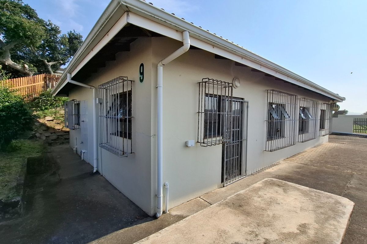 Rear exterior view of the townhouse featuring paved surrounds, security bars on windows, and a security gate, showing signs of exterior wear.