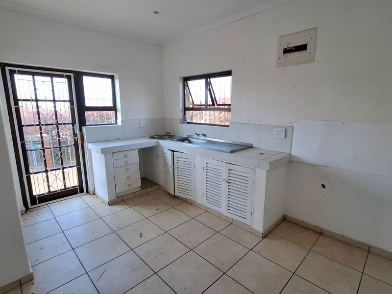An empty kitchen featuring tiled flooring, built-in cabinetry with a stainless steel sink, and direct access to the exterior via a security gate.