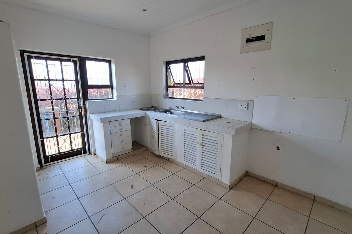An empty kitchen featuring tiled flooring, built-in cabinetry with a stainless steel sink, and direct access to the exterior via a security gate.