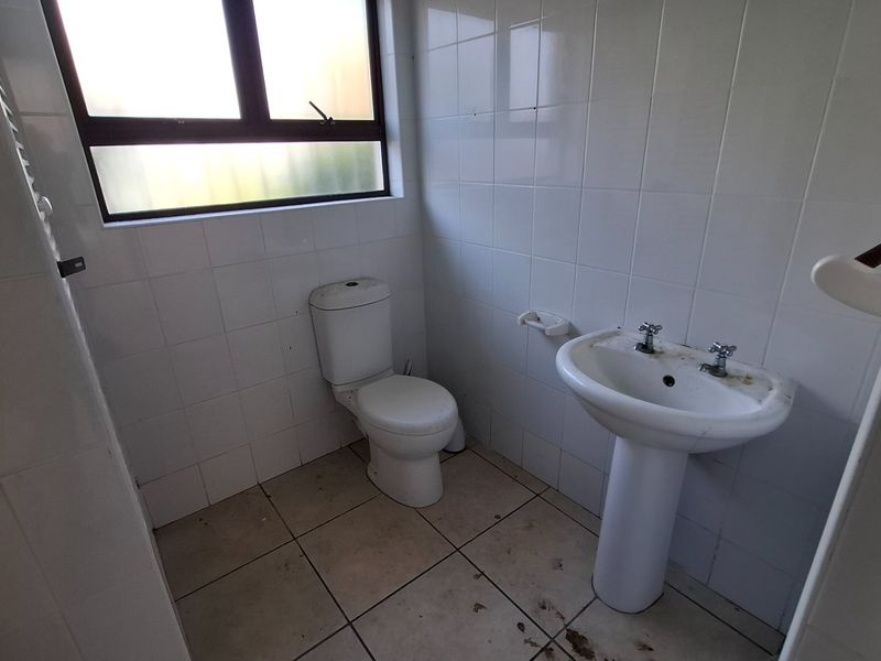 A compact bathroom featuring a pedestal basin, toilet, and tiled finishes, currently in need of cleaning and cosmetic updates.