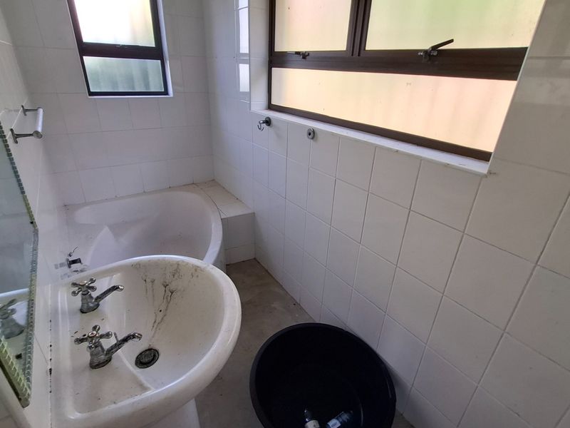 A dated bathroom featuring a pedestal basin and built-in bathtub with white wall tiling, requiring renovation and deep cleaning to restore functionality.