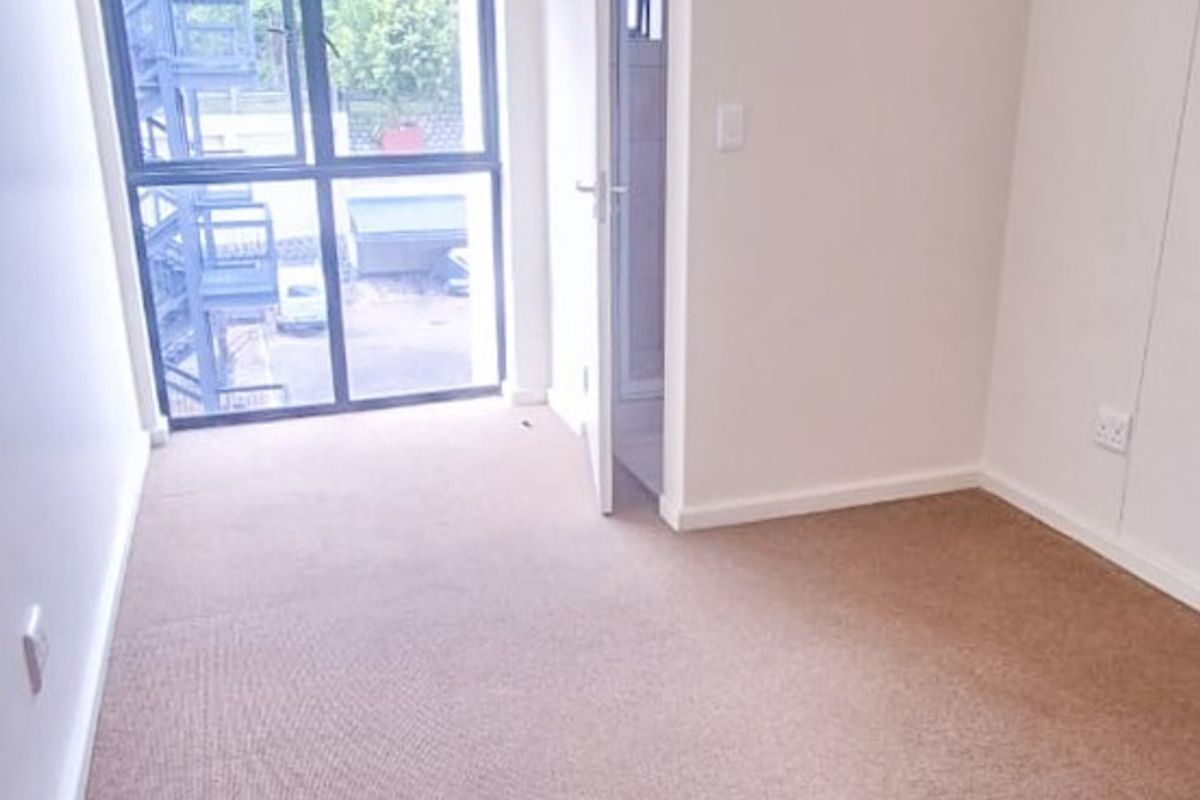 A bright, empty bedroom featuring neutral carpet flooring, clean white walls, and a large window with access to an external staircase.