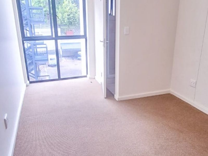 A bright, empty bedroom featuring neutral carpet flooring, clean white walls, and a large window with access to an external staircase.