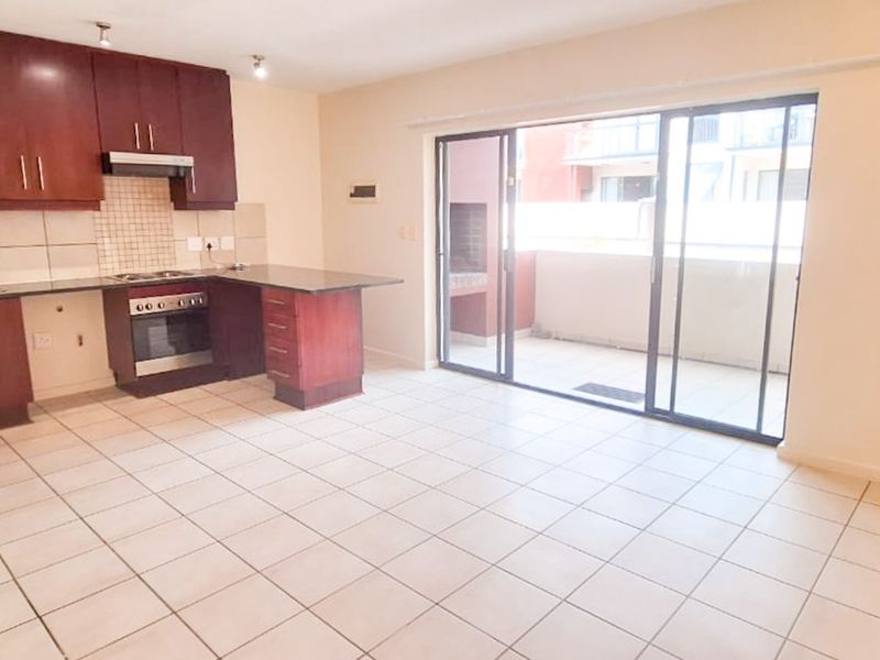 Open-plan kitchen and living area featuring dark wood cabinetry, granite countertops, tiled flooring, and sliding doors leading to a balcony with a built-in braai.