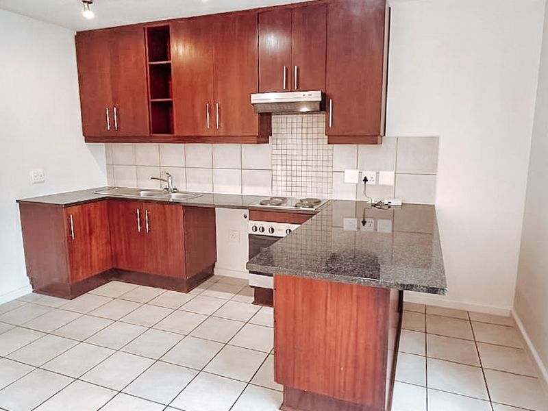 A functional kitchen featuring dark wood cabinetry, granite countertops, a tiled backsplash, and integrated electric hob with extractor fan.