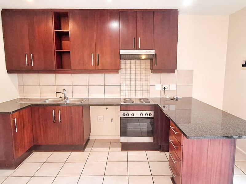 A clean, functional kitchen featuring dark wood cabinetry, granite countertops, built-in oven, hob, and extractor fan with a neutral tiled backsplash.