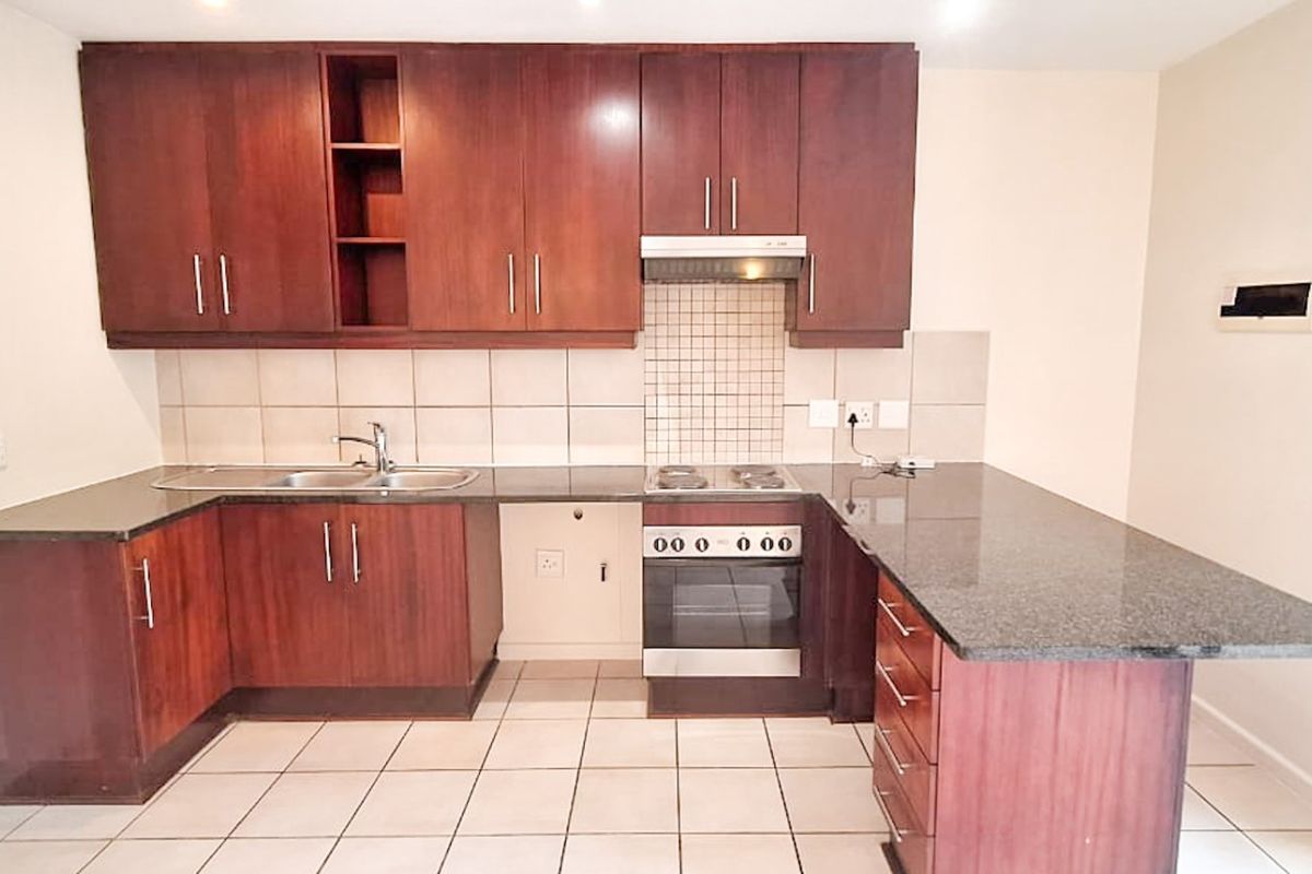 A clean, functional kitchen featuring dark wood cabinetry, granite countertops, built-in oven, hob, and extractor fan with a neutral tiled backsplash.