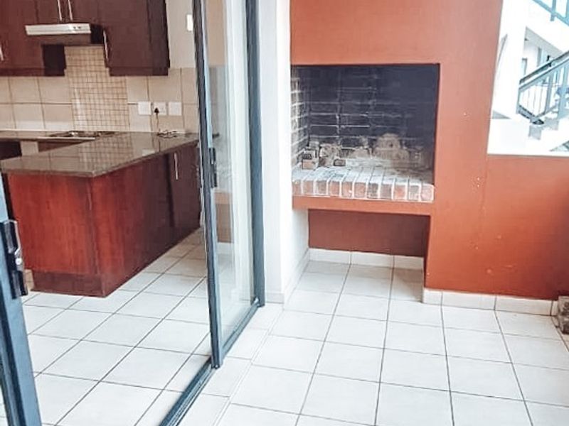 Covered balcony featuring a built-in brick braai, tiled flooring, and direct access to the kitchen through sliding glass doors.