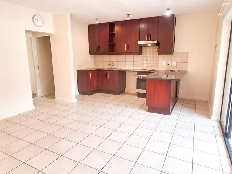 Open-plan kitchen and living area featuring dark wood cabinetry, granite countertops, tiled flooring, and direct access to a patio with a built-in braai.