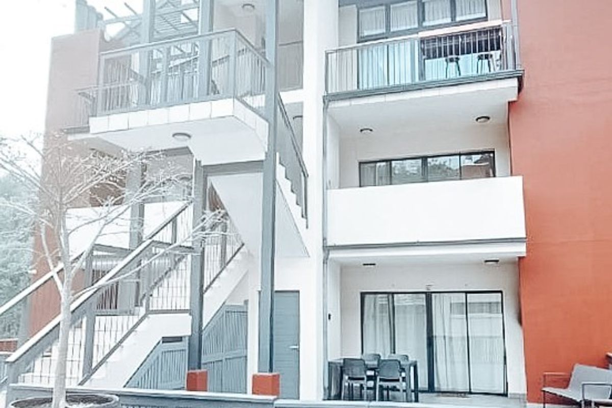 Rear view of a modern apartment building featuring multi-level balconies, external staircases, and a paved ground-floor patio area.