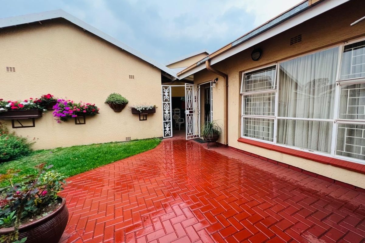 A well-maintained rear courtyard featuring red brick paving, security gates, and large windows with security bars, providing a clean and functional outdoor space.